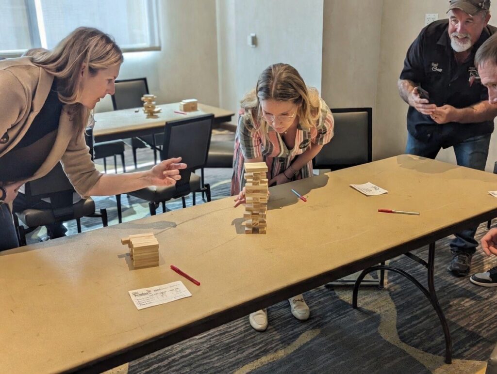 Woman placing a jenga block while another woman and two men look on hopeful she will place it correctly