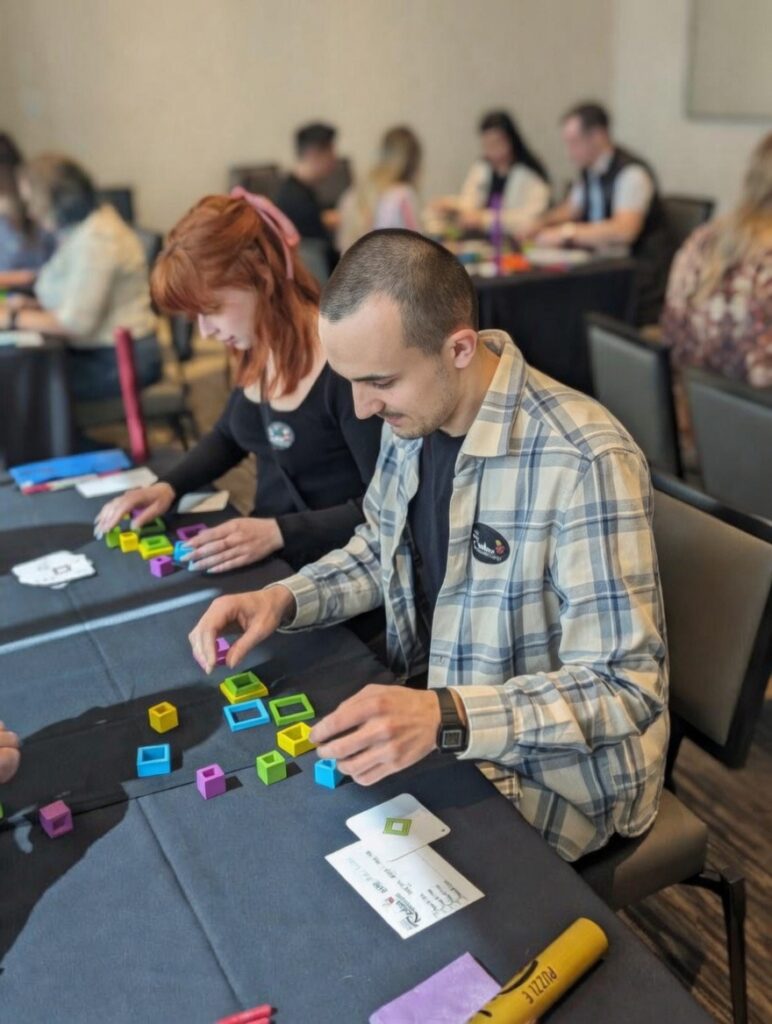 man and woman working with colored squares in a large room with others doing a workplace assessment