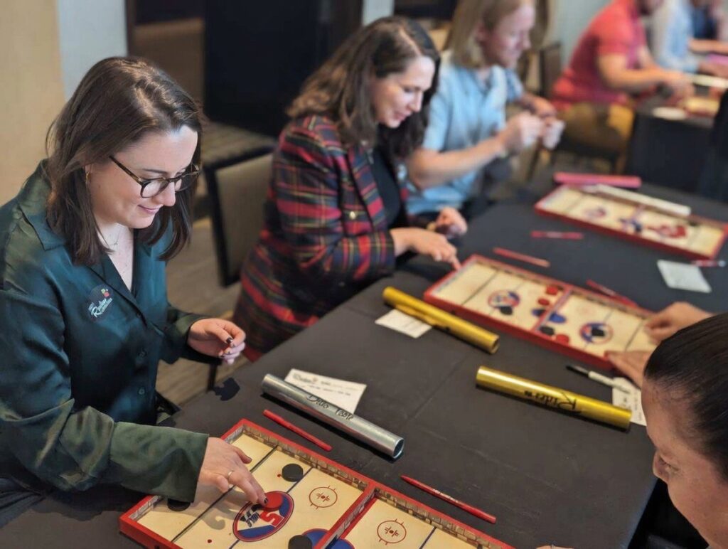 group of professional people engaging in a primitive table puck game at a workplace assessment